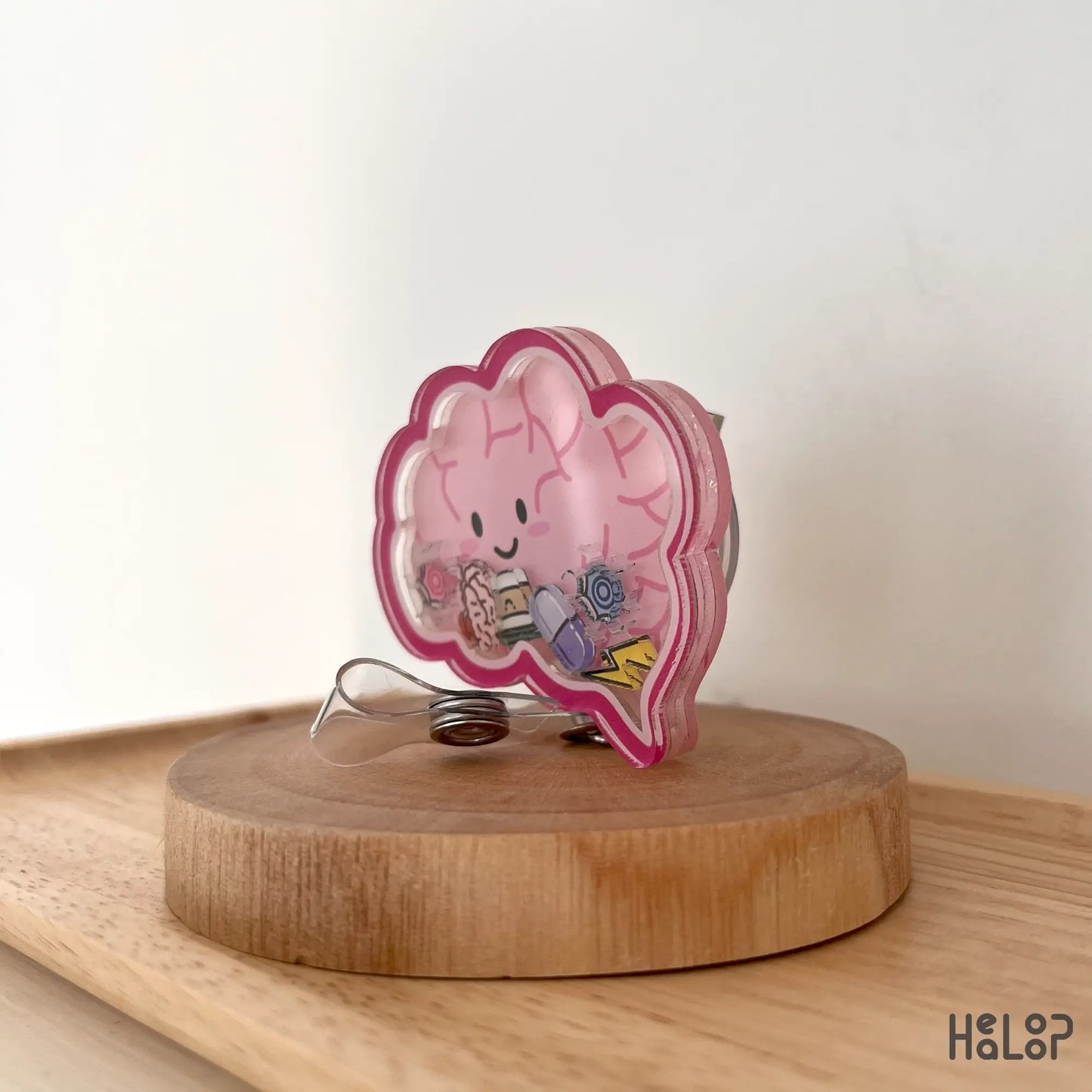 Side view of brain badge reel with floating charm details on pink background