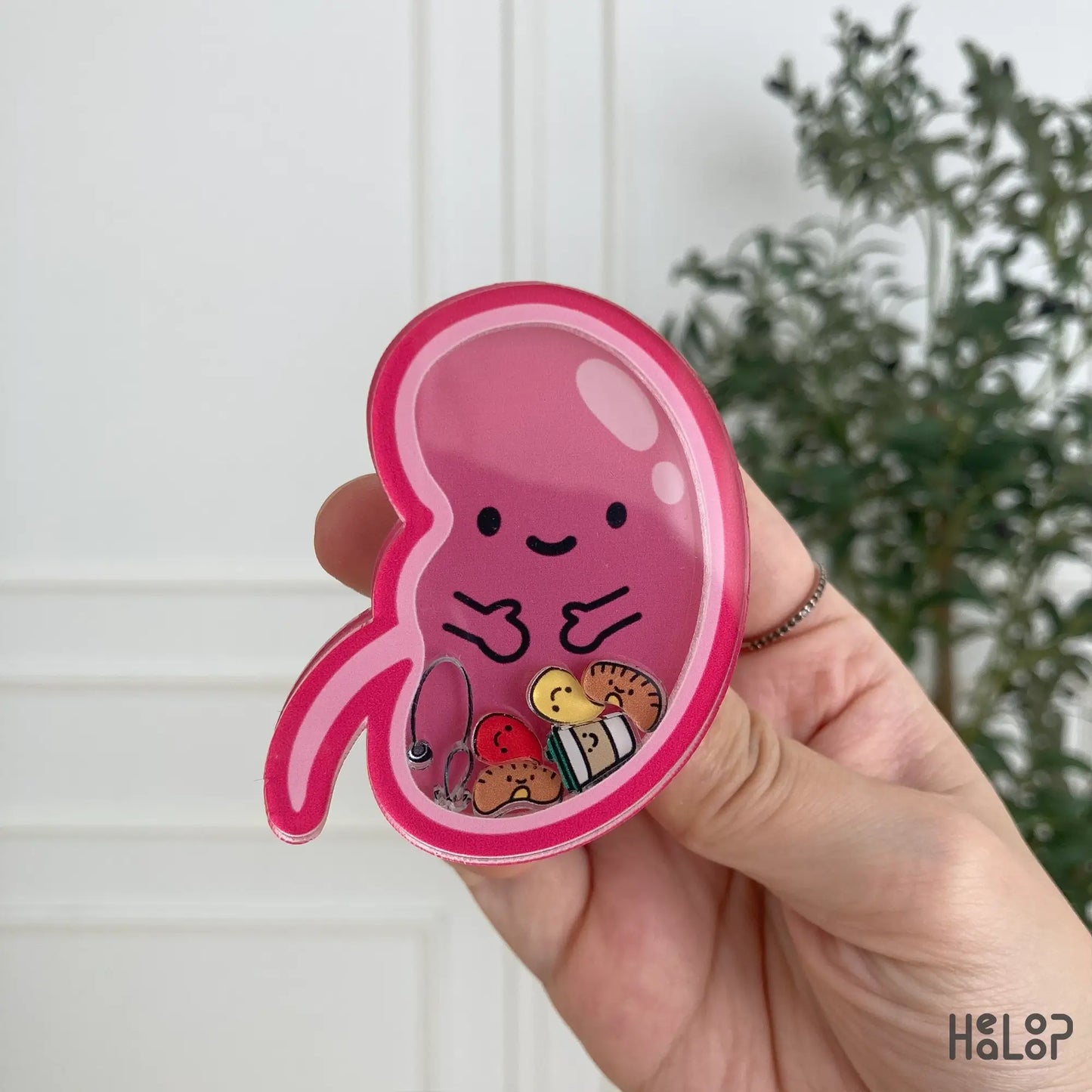Pink kidney-shaped shaker phone grip with floating mini charms, held in hand