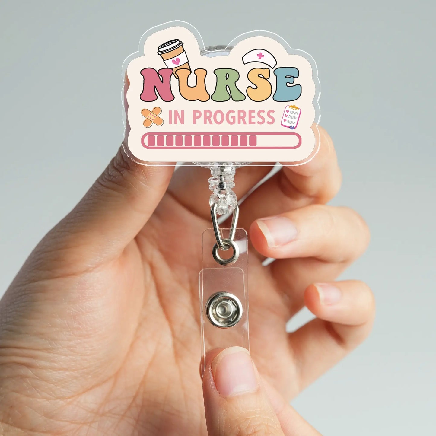 Hand holding a badge holder with 'Nurse In Progress' design against a gray background