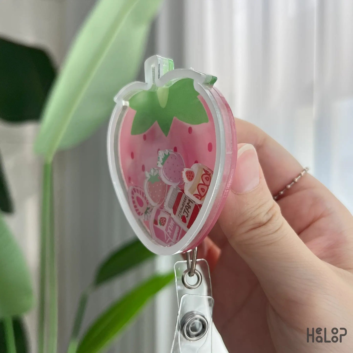 Angled view of strawberry shaker badge reel with kawaii floating fruit charms