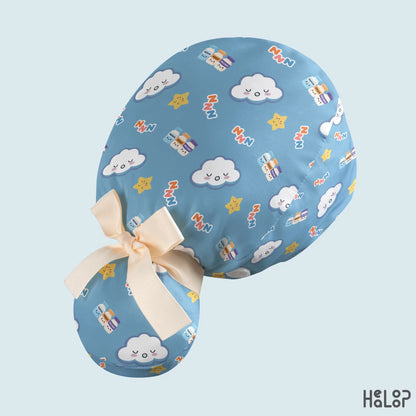 Blue anesthesia ponytail scrub cap angled back view displaying cute sleeping clouds, smiling stars, anesthesia medication vials, and a cream-colored ribbon bow.