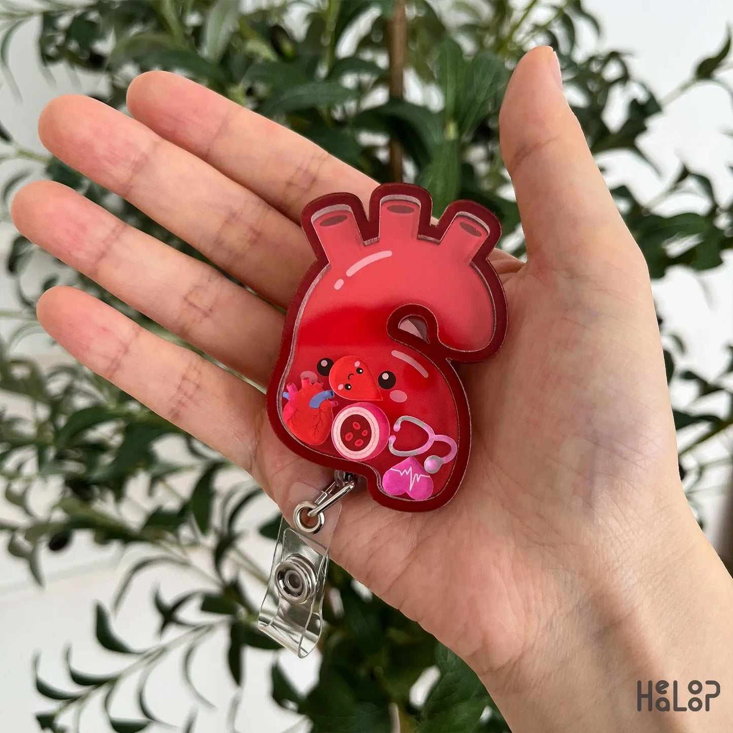 Aorta shaker badge reel with moving medical charms displayed in hand, designed for cardiac nurses and cardiology professionals.