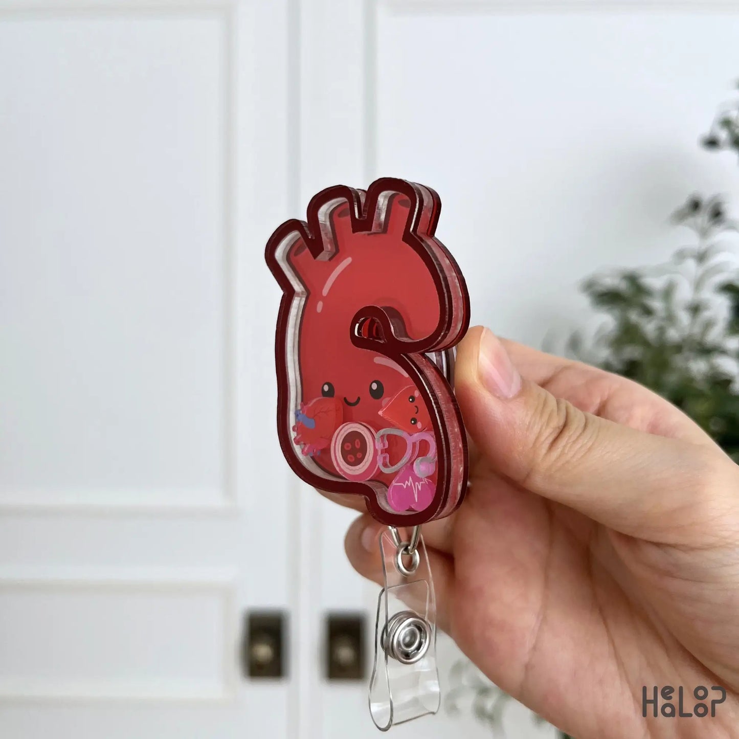 Side angle of a layered acrylic aorta shaker badge reel filled with cute medical and heart-themed charms.