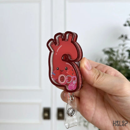 Side angle of a layered acrylic aorta shaker badge reel filled with cute medical and heart-themed charms.