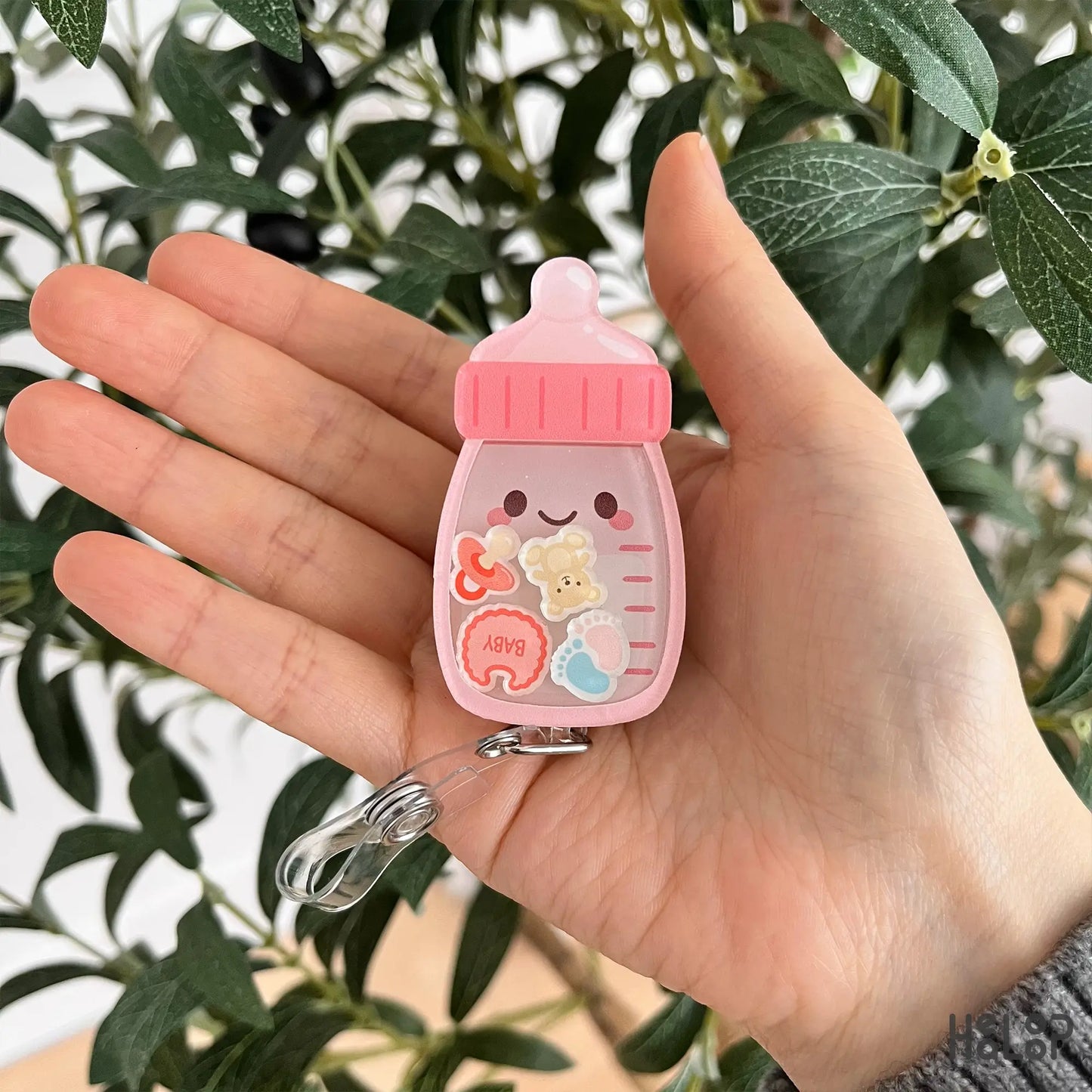 Baby bottle shaker badge reel shown in hand for size reference and everyday wear