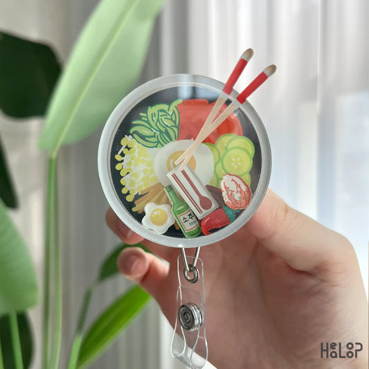 Detailed view of Korean bibimbap shaker badge reel with egg, soju, and vegetable charms