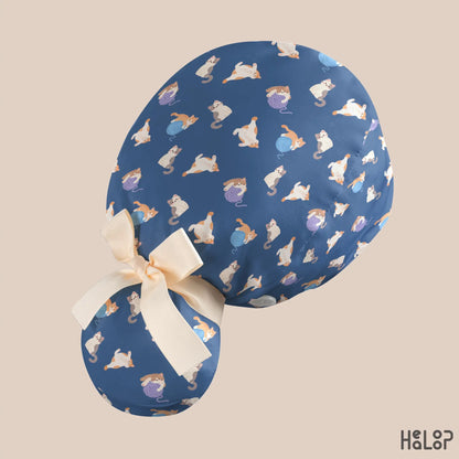 Angled back view of the HEALOOP Cat Ponytail Scrub Cap, highlighting the playful cat and yarn ball pattern, navy blue fabric, roomy hair pouch, and cream ribbon detail.