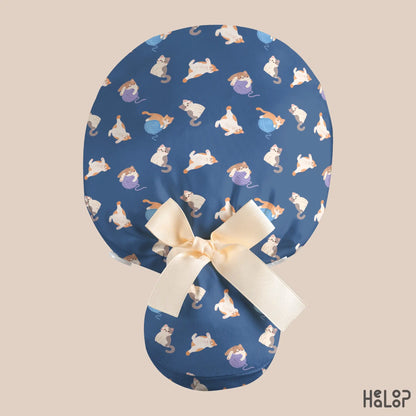 Cat Ponytail Scrub Cap shown from the back, featuring adorable cats and colorful yarn balls on navy blue fabric, with a spacious ponytail pouch and cream-colored ribbon bow.