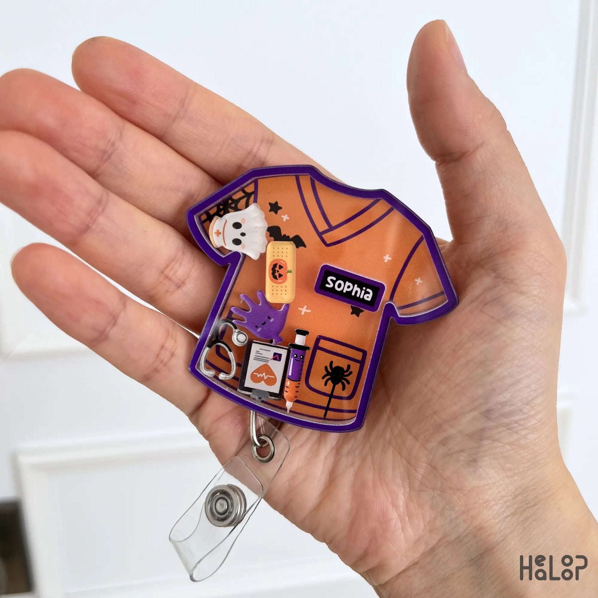 Custom Halloween nurse shaker badge reel with personalized name featuring spooky medical charms on an orange scrub top.