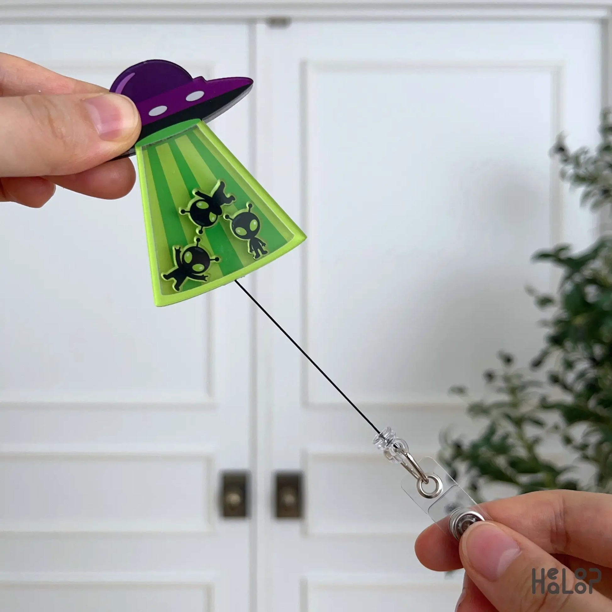 Cute Alien UFO Shaker Badge Reel with extended retractable cord demonstrating smooth pull and interactive shaker design.