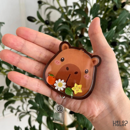 Cute Capybara shaker badge reel with movable flower, orange, leaf, and smiling star charms. Perfect retractable ID holder for nurses and animal lovers.