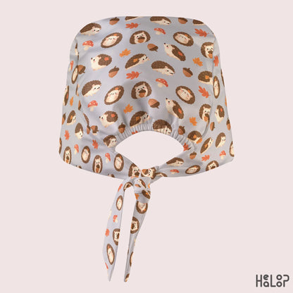 Hedgehog Classic Scrub Cap shown from the back, featuring cute hedgehogs, autumn leaves, acorns, and mushrooms on light gray fabric with an elastic opening and adjustable back ties.