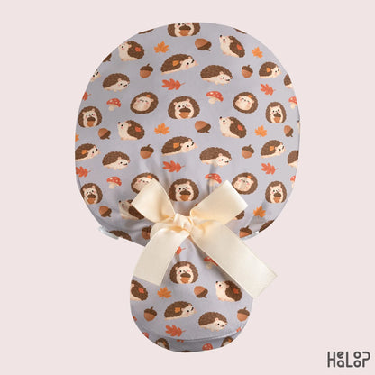 Hedgehog ponytail scrub cap with adorable woodland hedgehog pattern, fall leaves, acorns, mushrooms, and cream ribbon bow on the back.