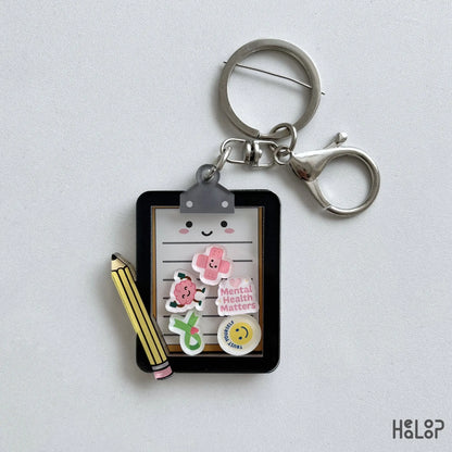 Cute Mental Health Board Shaker Keychain featuring a clipboard, pencil, and colorful moving mental health charms.