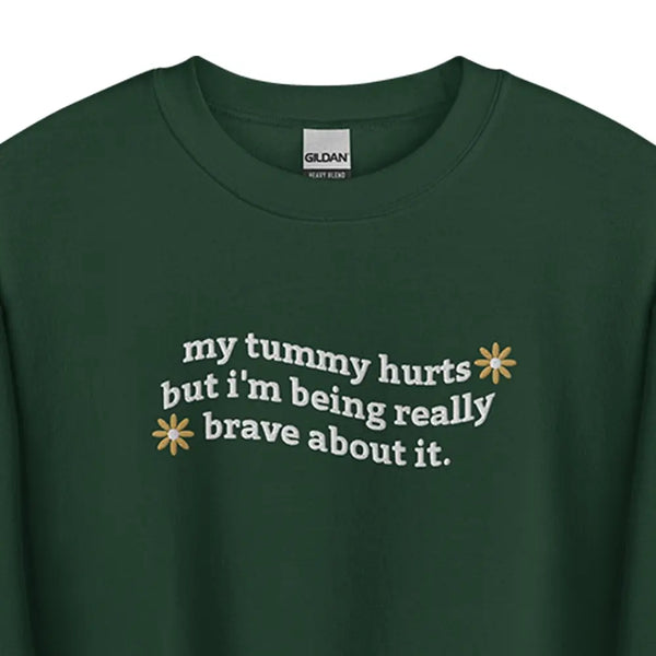 Flat lay of My Tummy Hurts sweatshirt in Forest Green with embroidered text, 'My tummy hurts but I'm being really brave about it' zoom