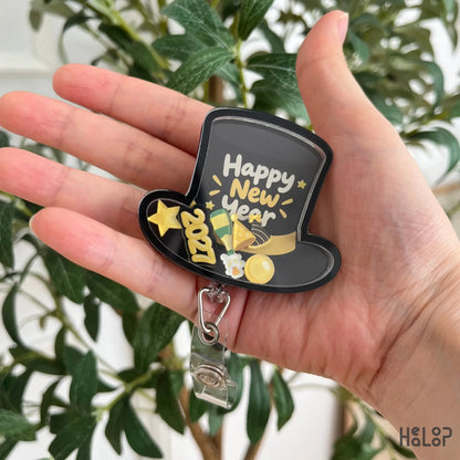 Happy New Year 2027 shaker badge reel displayed in hand, showing the black top hat shape, gold 2027 charm, and festive details.