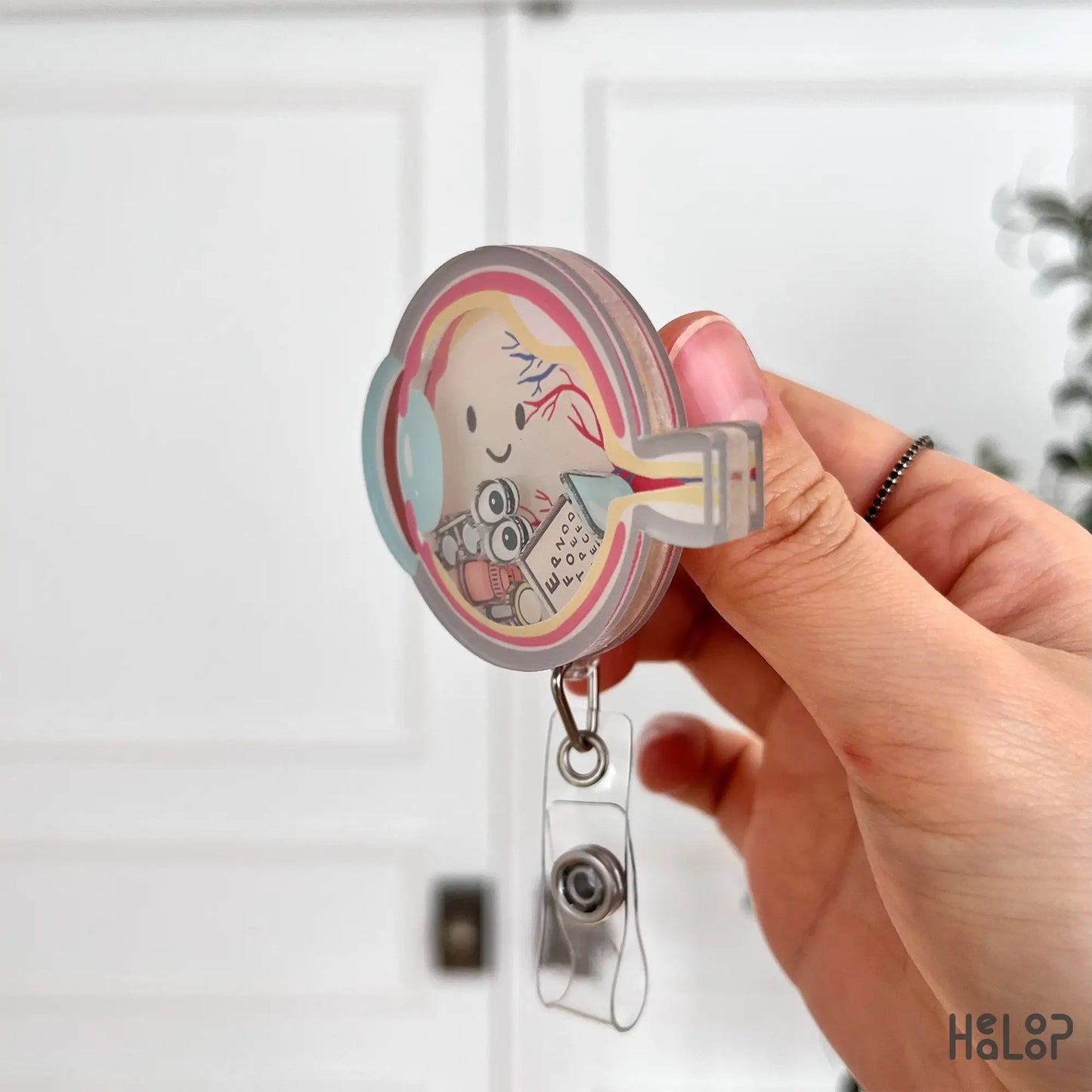 Layered acrylic ophthalmology shaker badge reel shown from side angle with clear retractable clip.