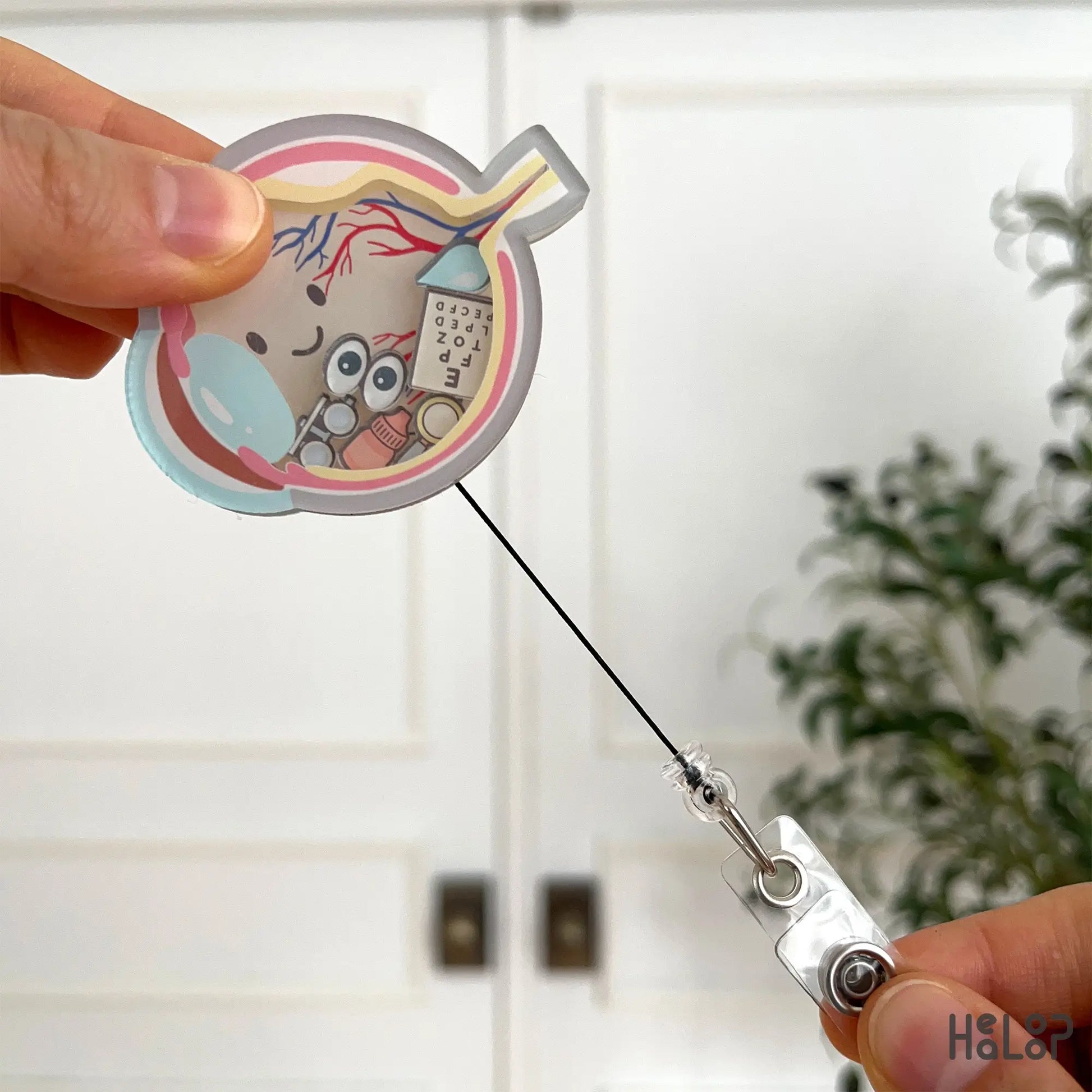 Retractable ophthalmology badge holder with eye chart and optic-themed shaker pieces.