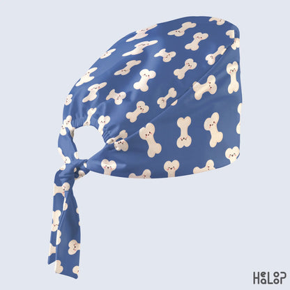 Ortho Bone Classic Scrub Cap shown at an angle with cute cream-colored bone patterns, blue fabric and matching adjustable back ties.