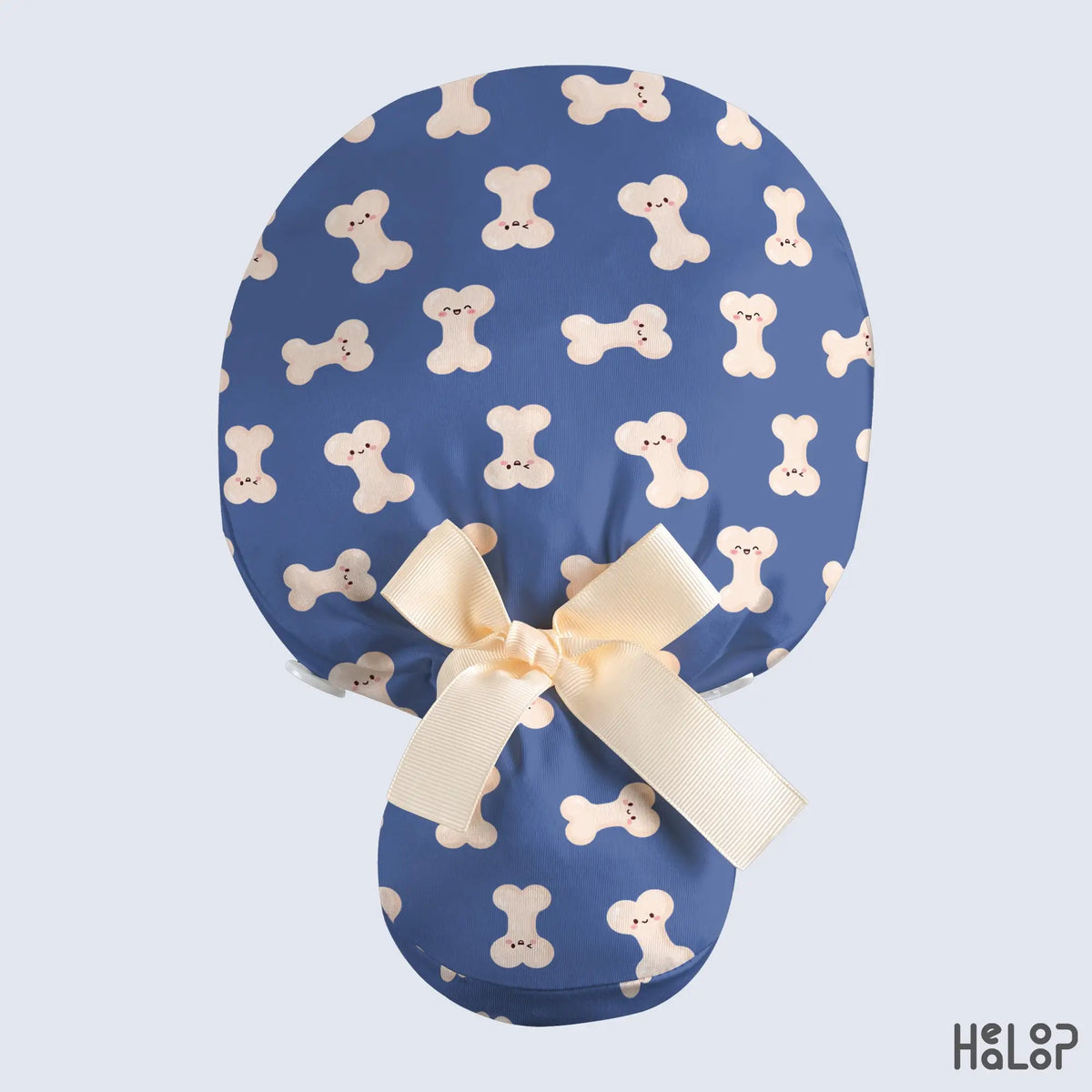 Ortho Bone Ponytail Scrub Cap in blue with cute smiling bone patterns, a cream ribbon bow, and a spacious ponytail pouch, shown from the back.