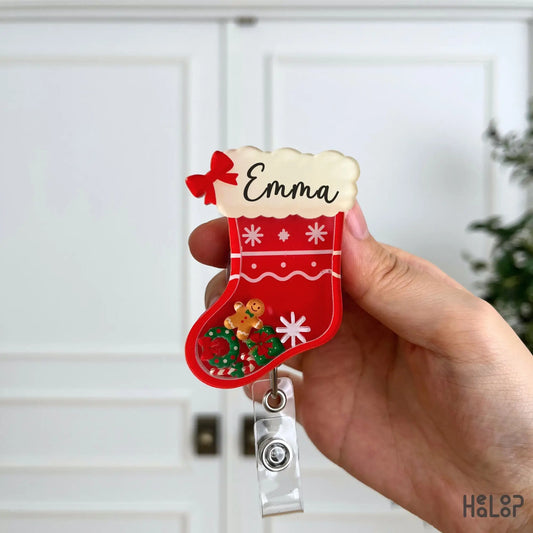 Front close-up of a personalized Christmas stocking shaker badge reel featuring festive Christmas charms and a custom name.