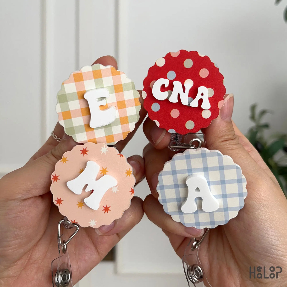 Personalized badge reels with custom letters E, M, A and CNA on colorful patterned backgrounds