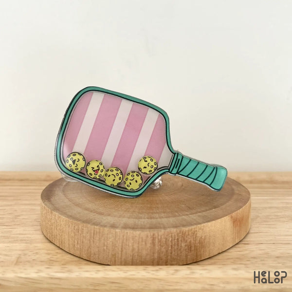 Angled view of cute pink paddle badge reel with floating pickleballs