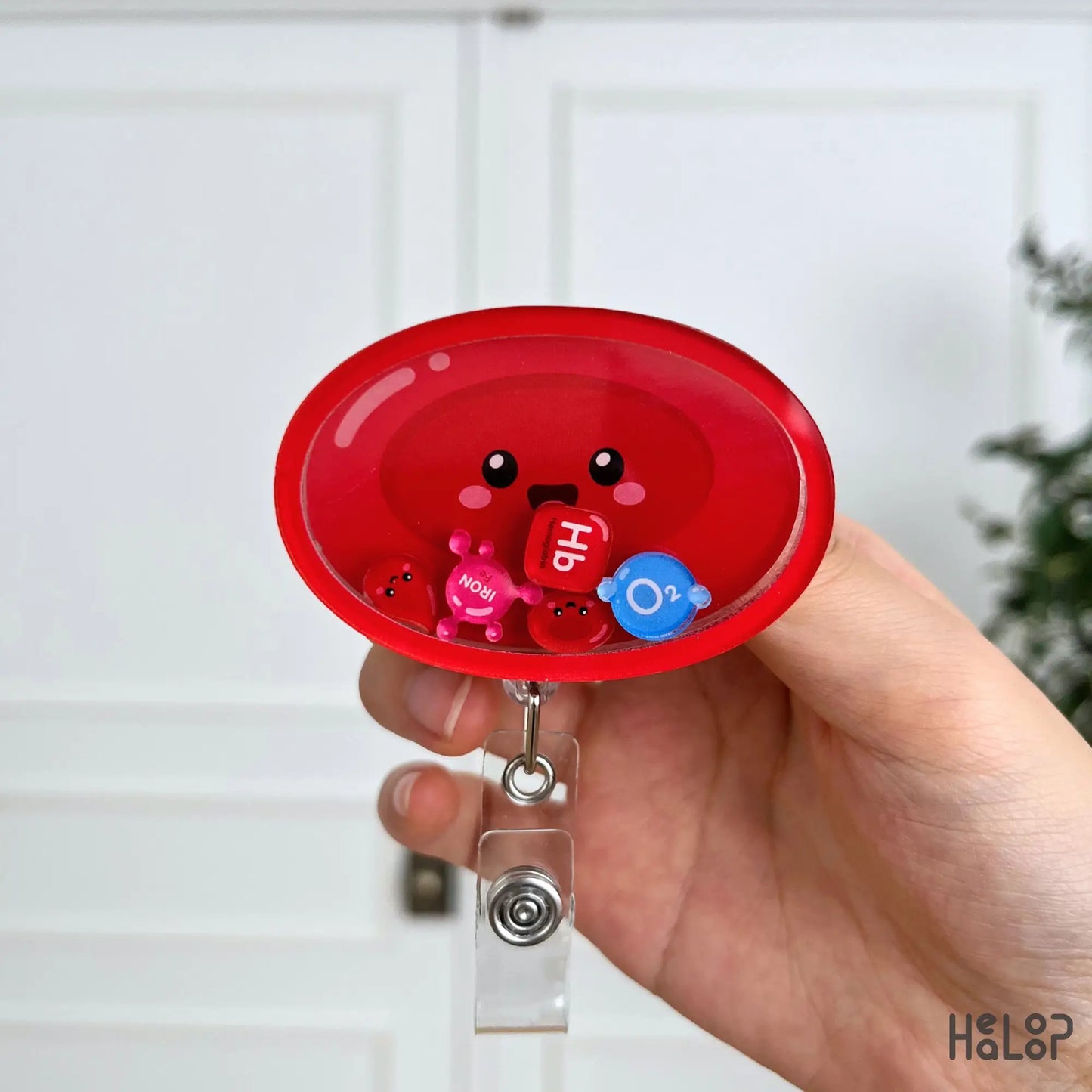 Cute Red Blood Cell Shaker Badge Reel displayed in hand, featuring movable Hb, iron, O₂, and red blood cell charms for healthcare professionals.
