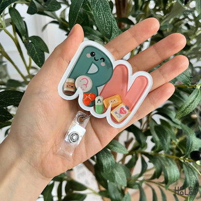 Close-up handheld view of RN shaker badge reel showing detailed nursing-themed artwork.