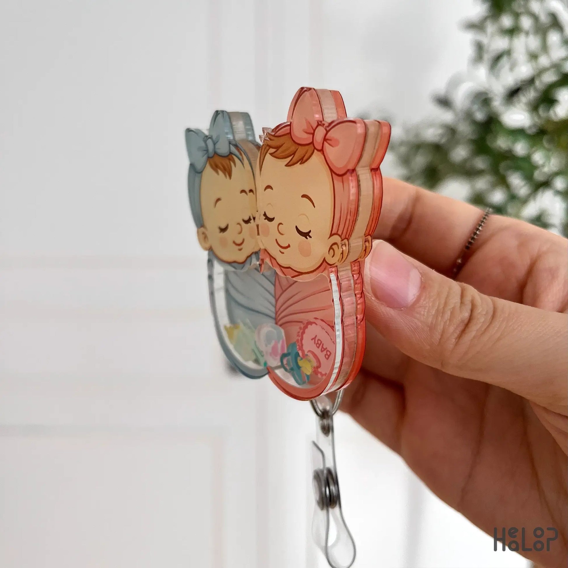 Side view of Healoop swaddle baby shaker badge reel showing 3D acrylic layers and alligator clip