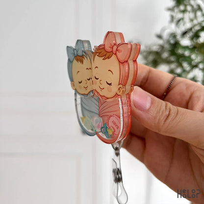 Side view of Healoop swaddle baby shaker badge reel showing 3D acrylic layers and alligator clip