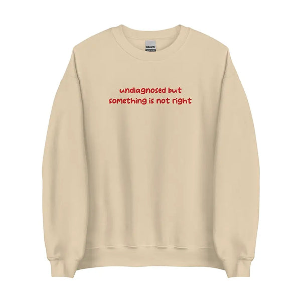 Sand-colored sweatshirt with 'undiagnosed but something is not right' embroidered in red, displayed flat for a detailed view.