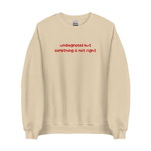 Sand-colored sweatshirt with 'undiagnosed but something is not right' embroidered in red, displayed flat for a detailed view.