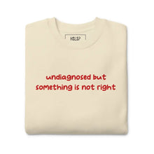 Folded Bone-colored sweatshirt with 'undiagnosed but something is not right' embroidered in red, highlighting mental health.