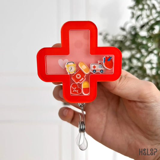 Urgent care shaker badge reel with red cross shape, floating ambulance, and pill charms